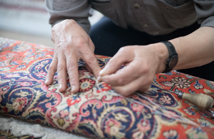 A skilled worker meticulously repairs a damaged rug